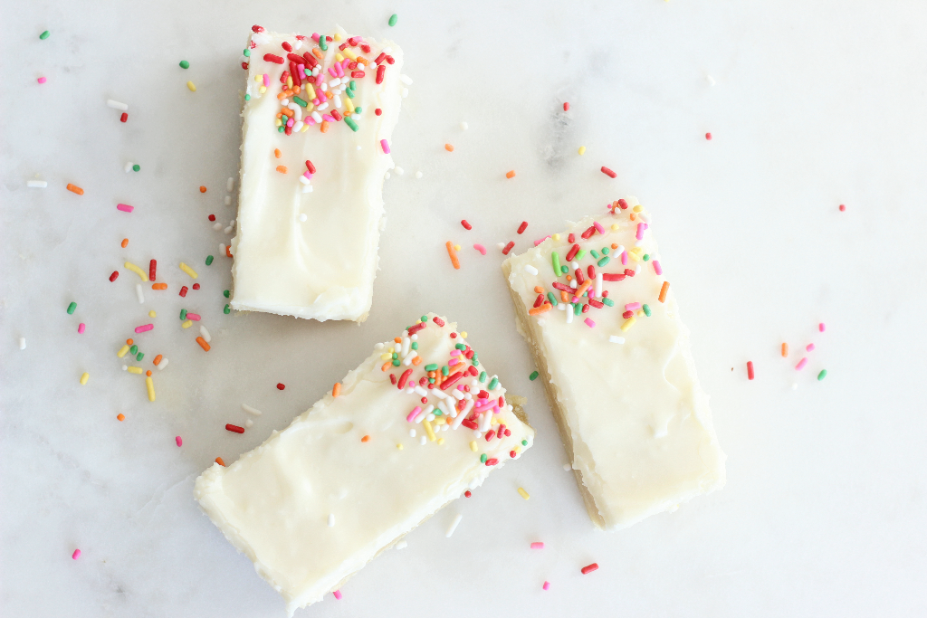 sugar cookie bars with cream cheese frosting with red sprinkles on a red plate