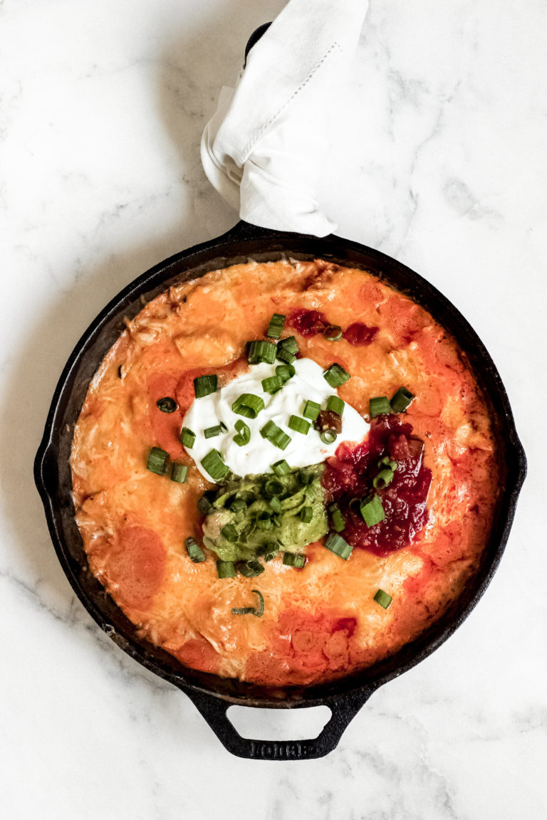 Overhead look of a skillet filled with all the best stuff of an enchilad and topped with sour cream, salsa and guacamole