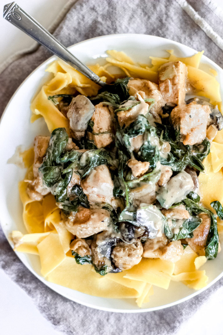 Overhead look at a plate full of pasta ribbons and a creamy sauce covering chicken and mushrooms and spinach