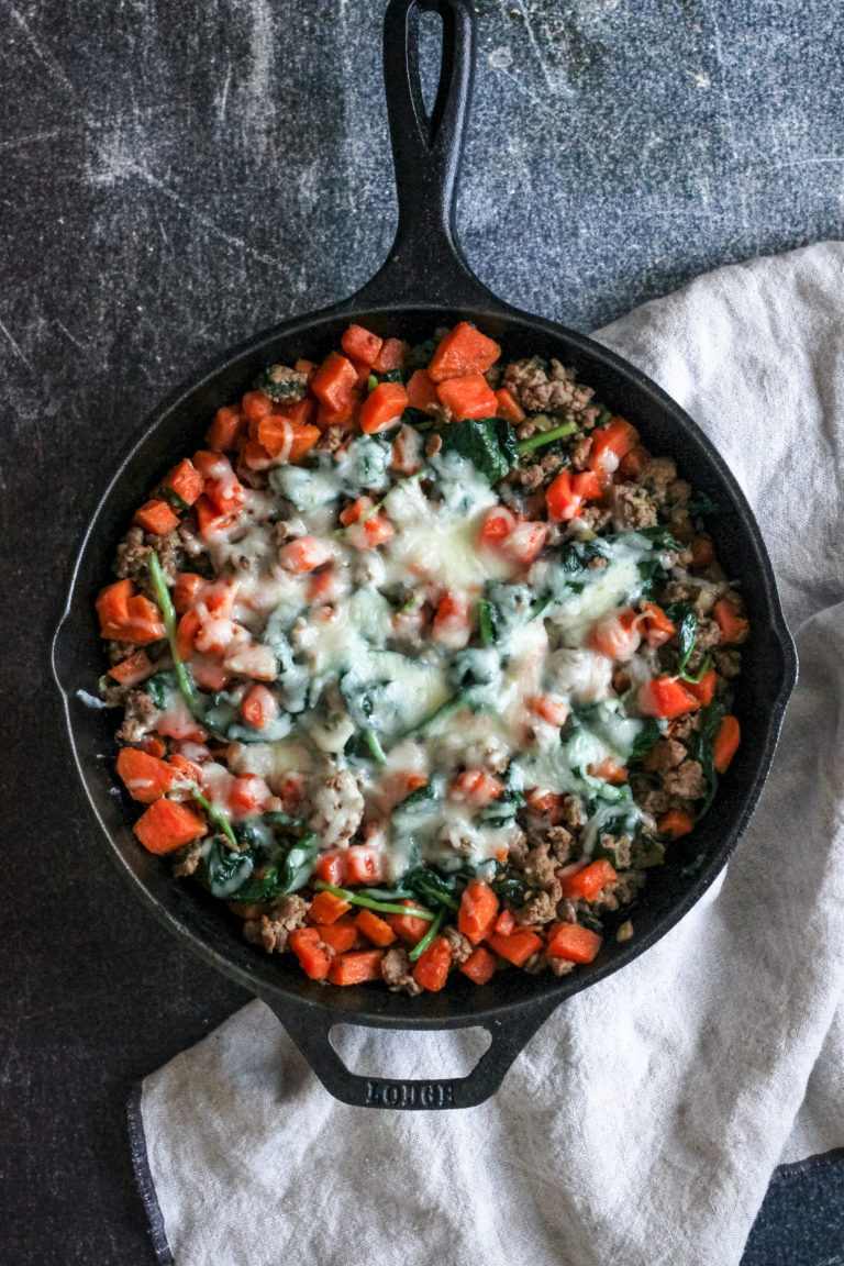 overhead view of a skillet filled with sausage, sweet potatoes, spinach and lots of cheese.