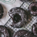 Overhead view of a baked chocolate donut with a vanilla glaze on a cooling rack