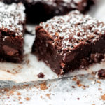 Shot of a dark chocolate brownie with chocolate chips inside topped with powdered sugar
