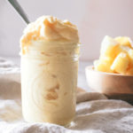 Three ingredient dole whip piled into a mason jar with chunks of fresh pineapple behind.