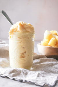 Three ingredient dole whip piled into a mason jar with chunks of fresh pineapple behind.