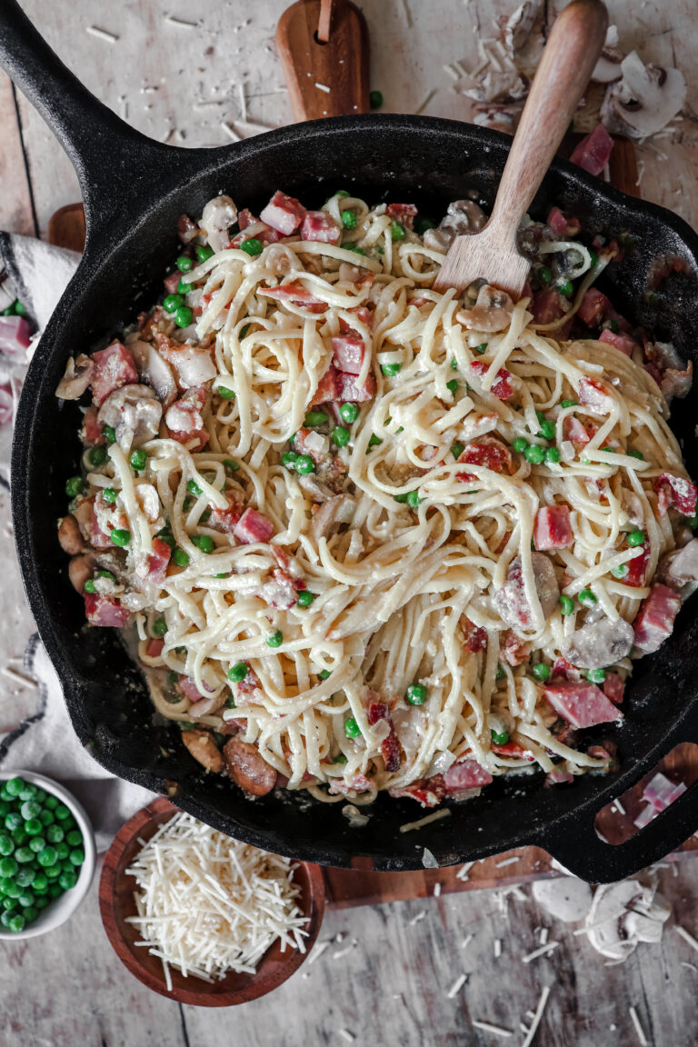 Overhead look at a skillet fill of linguine filled with noodles, bacon, mushrooms, peas and lots of cheese