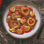 overhead view of a plate of toasted ravioli with hearts cut out on red sauce