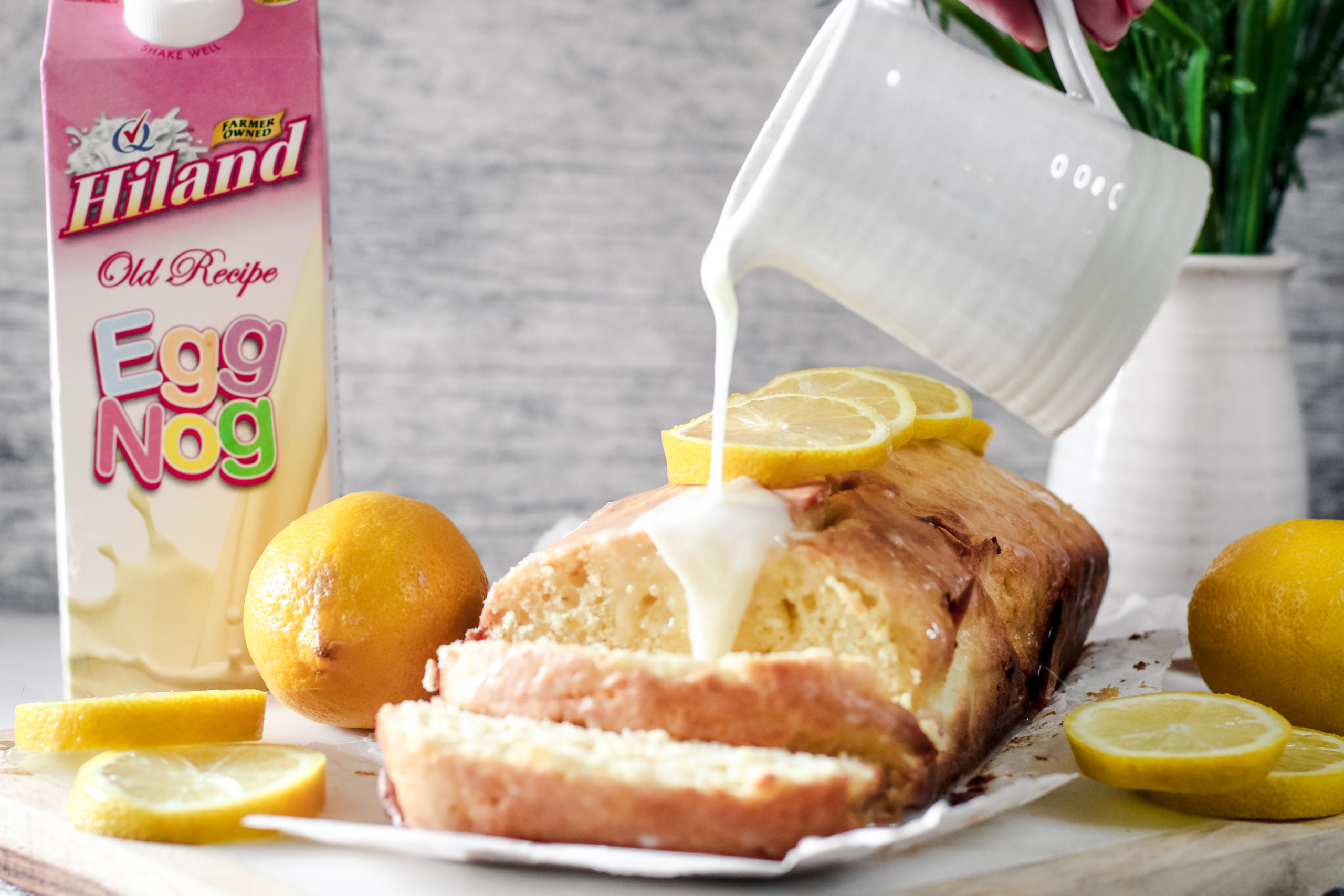 Eggnog Pound Cake Sliced open with lemons on top and glaze being poured