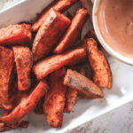 Overhead view of sweet potato wedges in the air fryer and dipping sauce