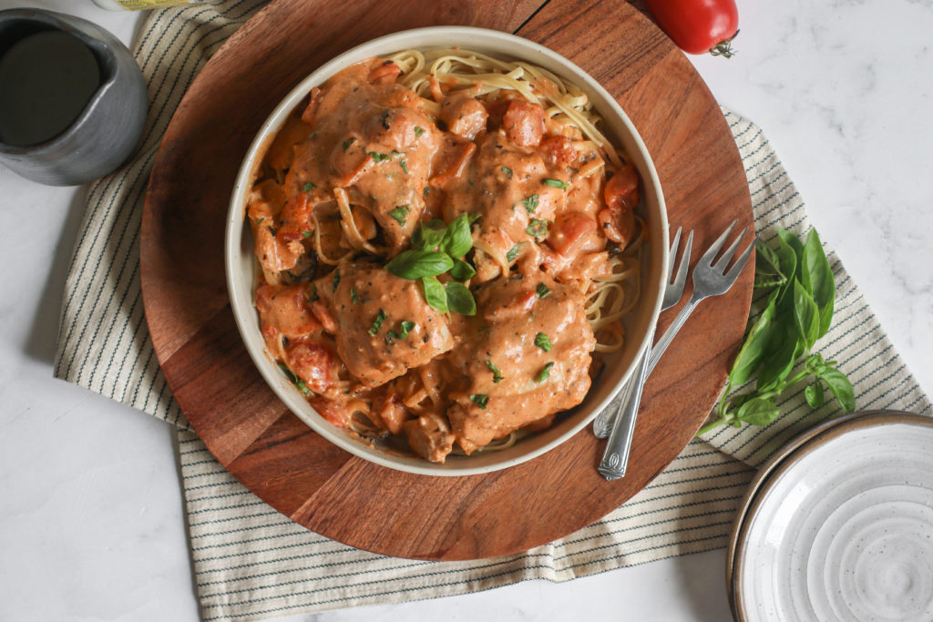 overhead view of a platter of slow cooker tomato basil chicken over noodles