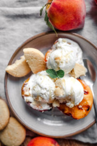 Grilled peach halves topped with scoops of vanilla ice cream on a white plate, served with a drizzle of honey and cookie crumbles