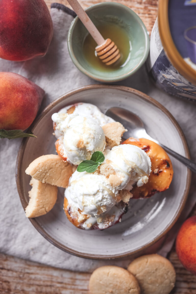 Grilled peach halves topped with scoops of vanilla ice cream served with drizzle of honey and cookie crumbles