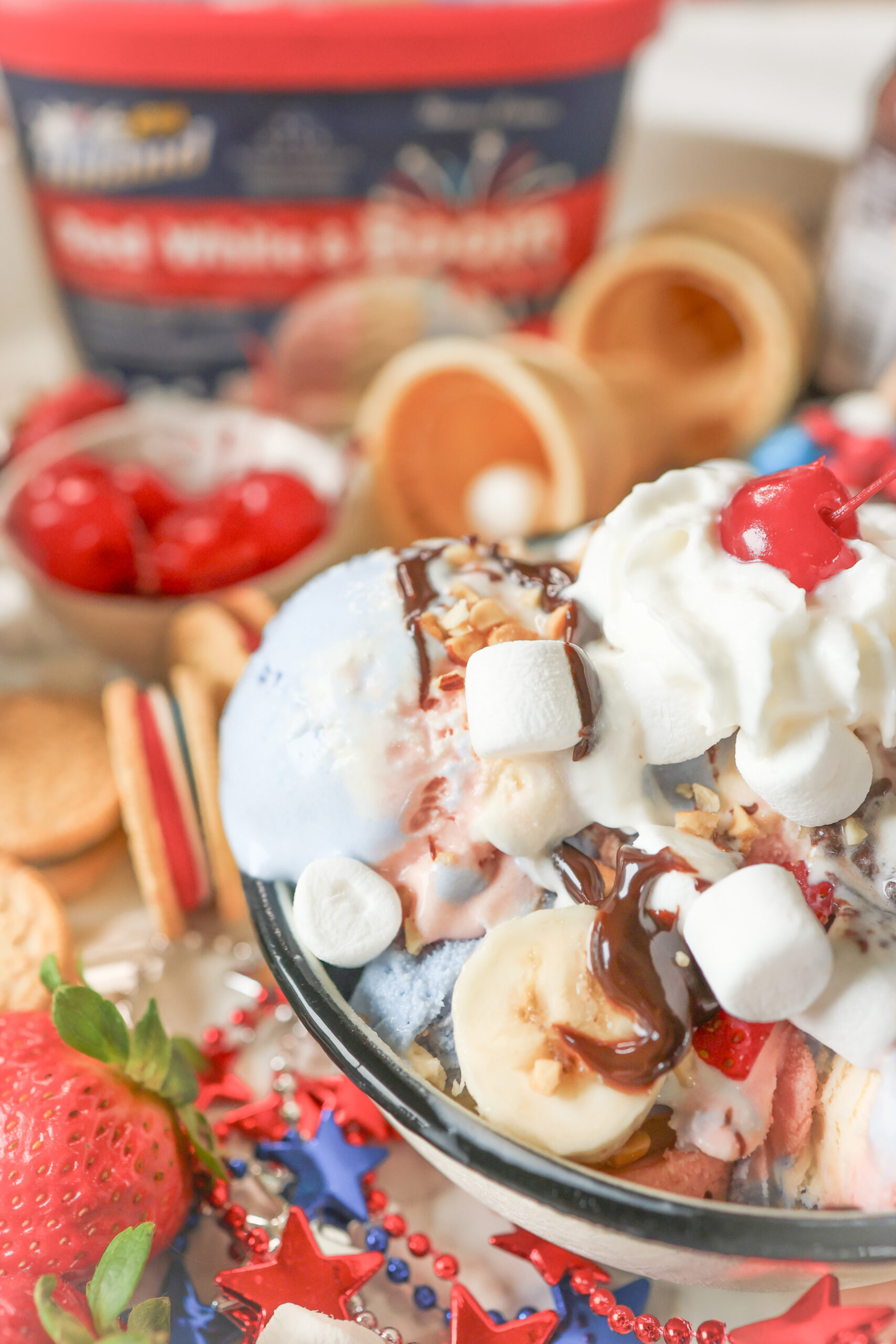 4th of July ice cream sundae board with Hiland Dairy Red White and Boom ice cream surrounded by colorful toppings including hot fudge, sprinkles, strawberries, blueberries, and whipped cream