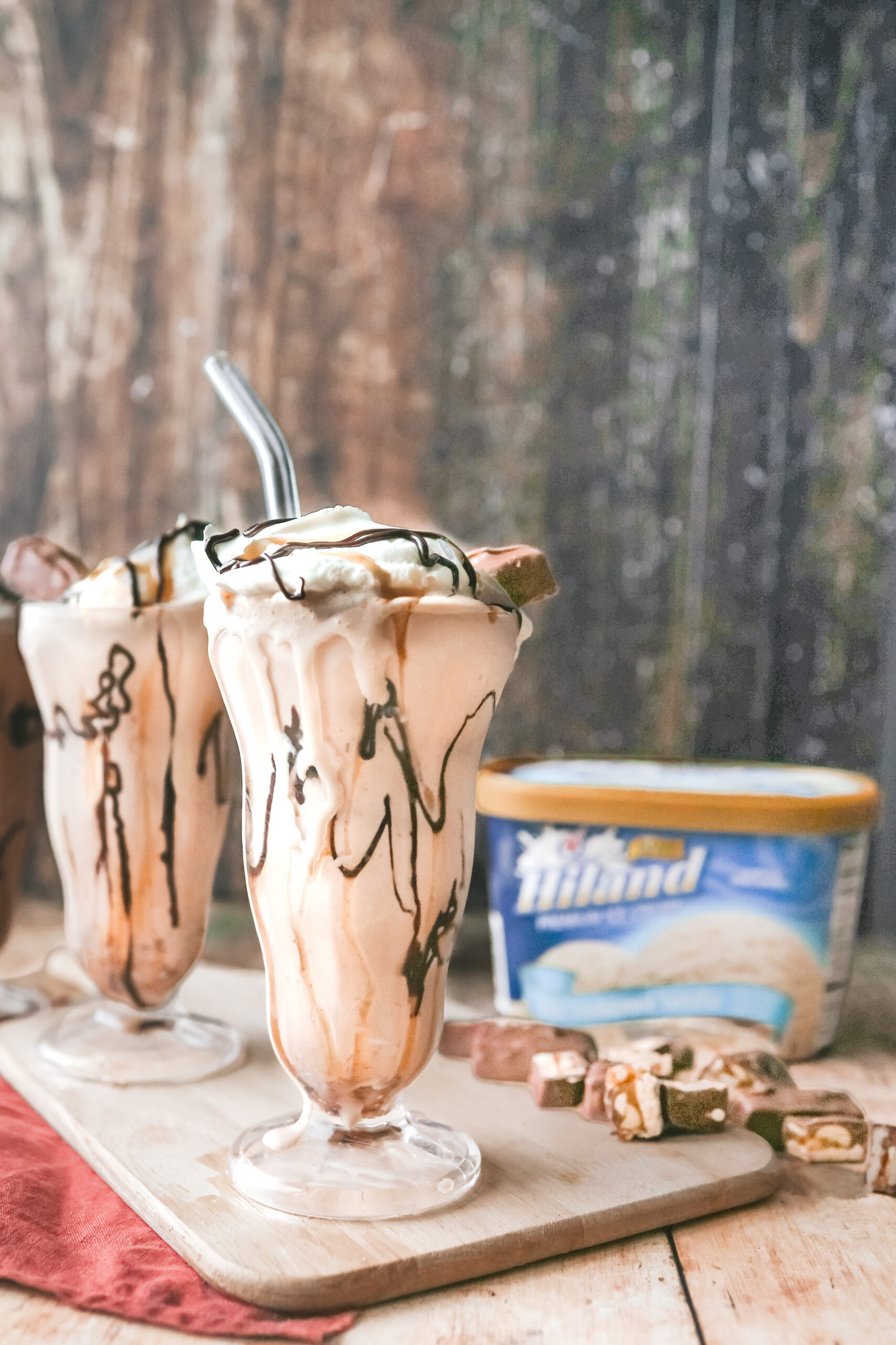 A straight on shot of 3 milkshake glasses filled with a snickers milkshake topped with chocolate drizzle and a snickers bite