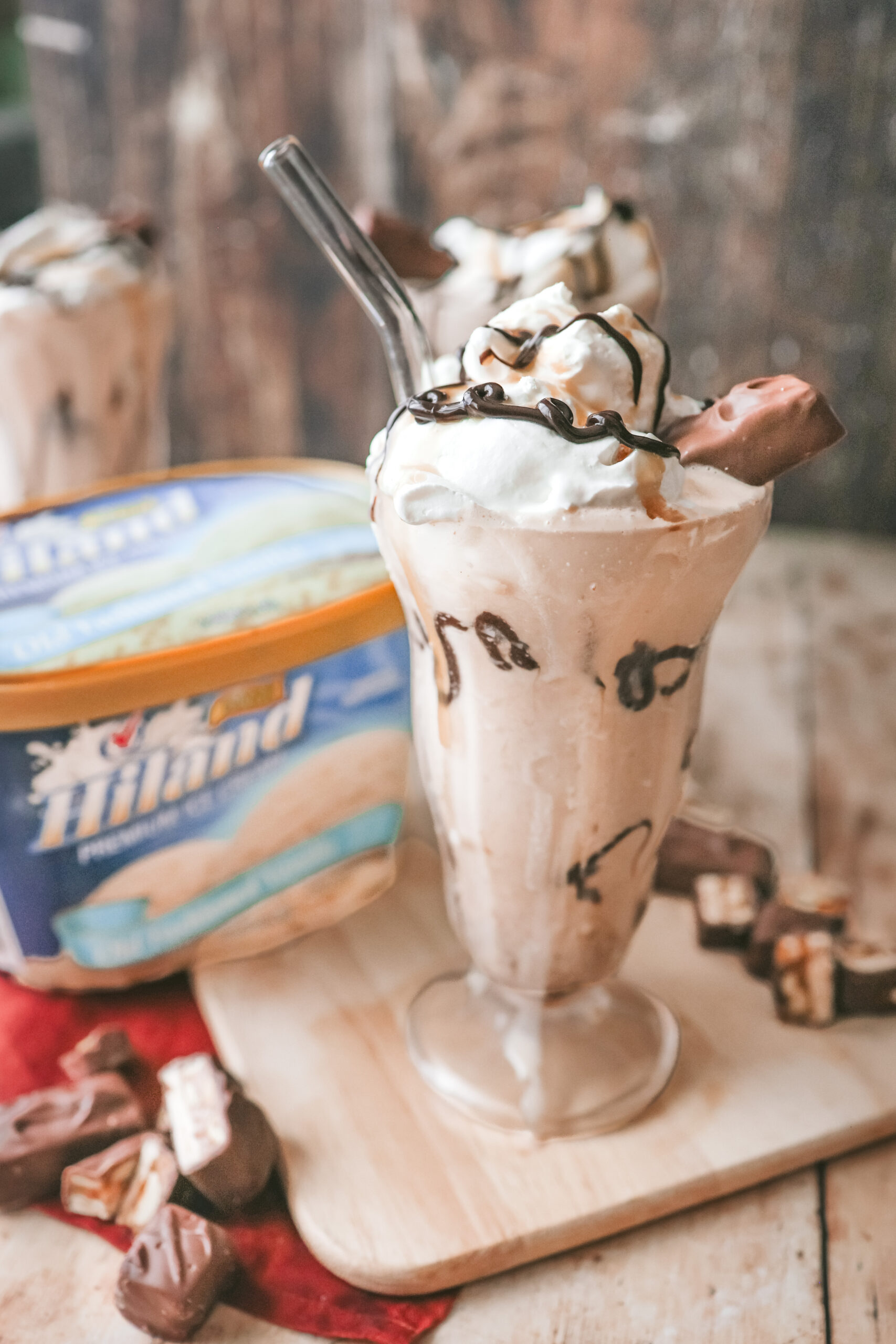 A straight on shot of 3 milkshake glasses filled with a snickers milkshake topped with chocolate drizzle and a snickers bite