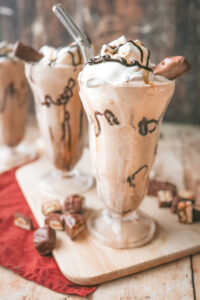 A straight on shot of 3 milkshake glasses filled with a snickers milkshake topped with chocolate drizzle and a snickers bite
