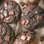 Chocolate peanut butter muffins with chocolate chips and a creamy peanut butter filling in the center, displayed on a plate.