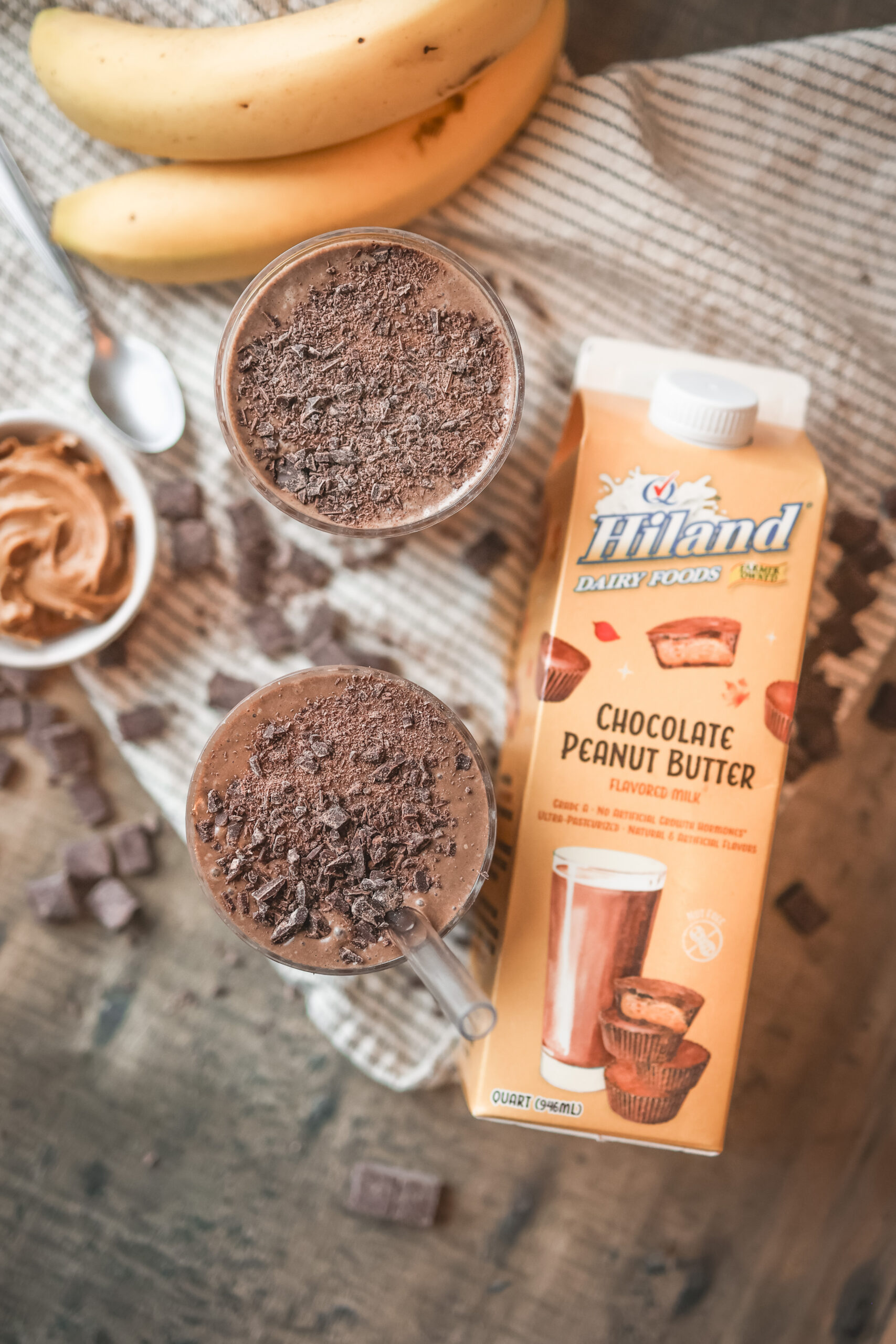 Ingredients for a chocolate peanut butter smoothie including chocolate peanut butter milk, frozen banana, peanut butter, cocoa powder, and vanilla extract.