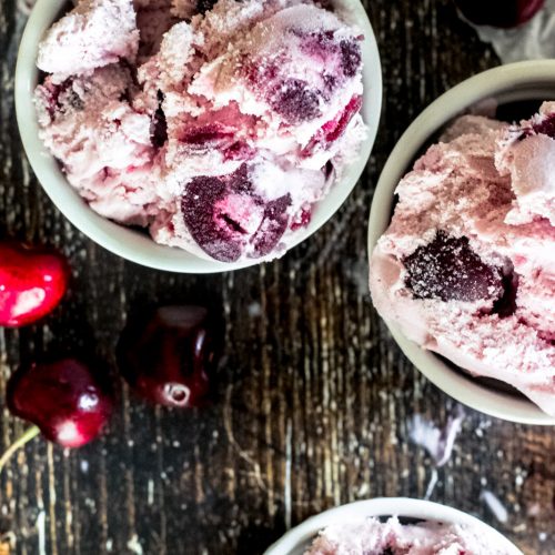 No churn black cherry ice cream scooped into a bowl with fresh black cherries
